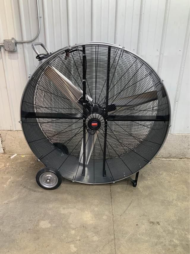 A large fan with wheels is sitting on the ground in front of a building.