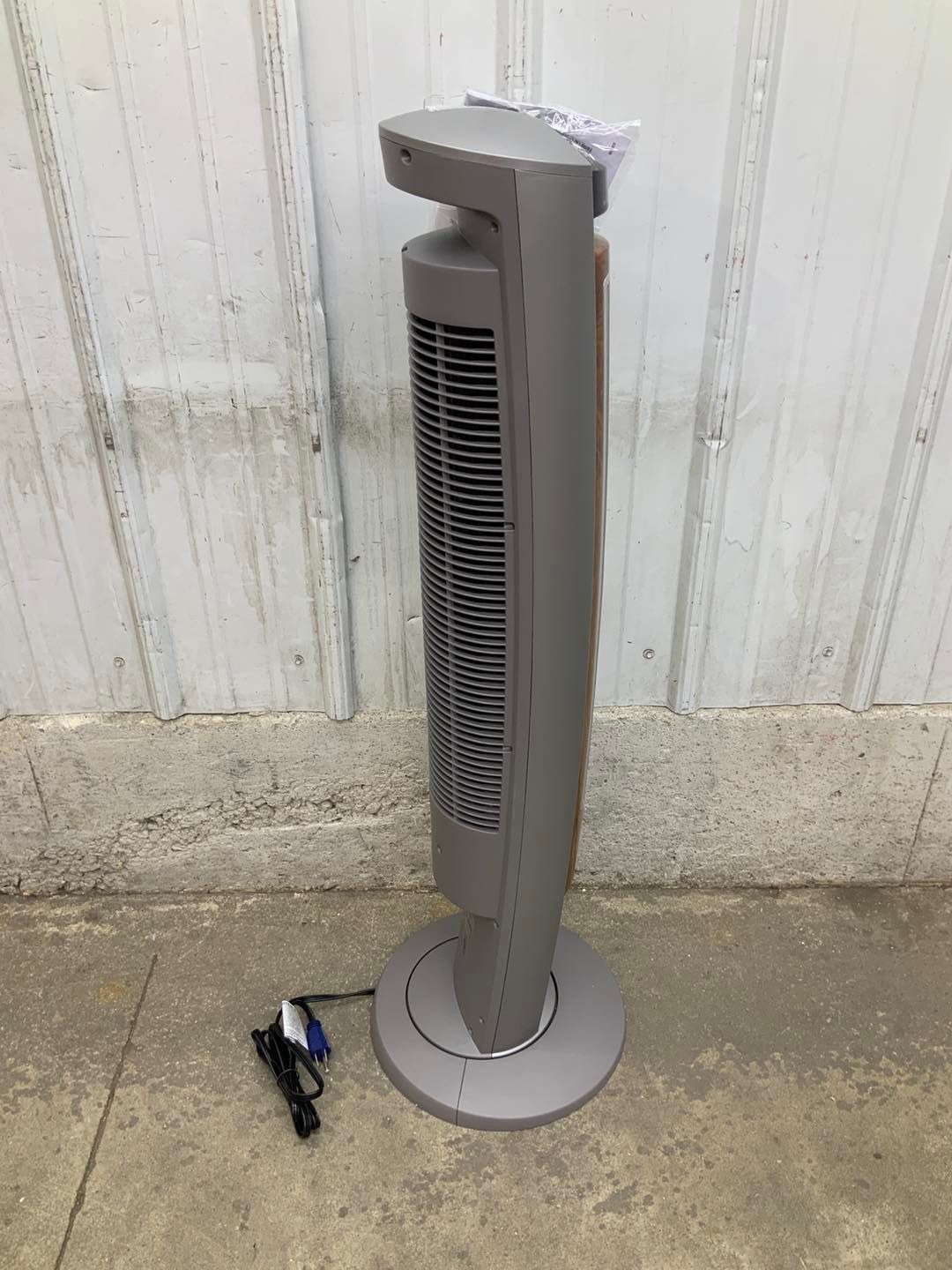 A tower fan is sitting on the ground next to a wall.