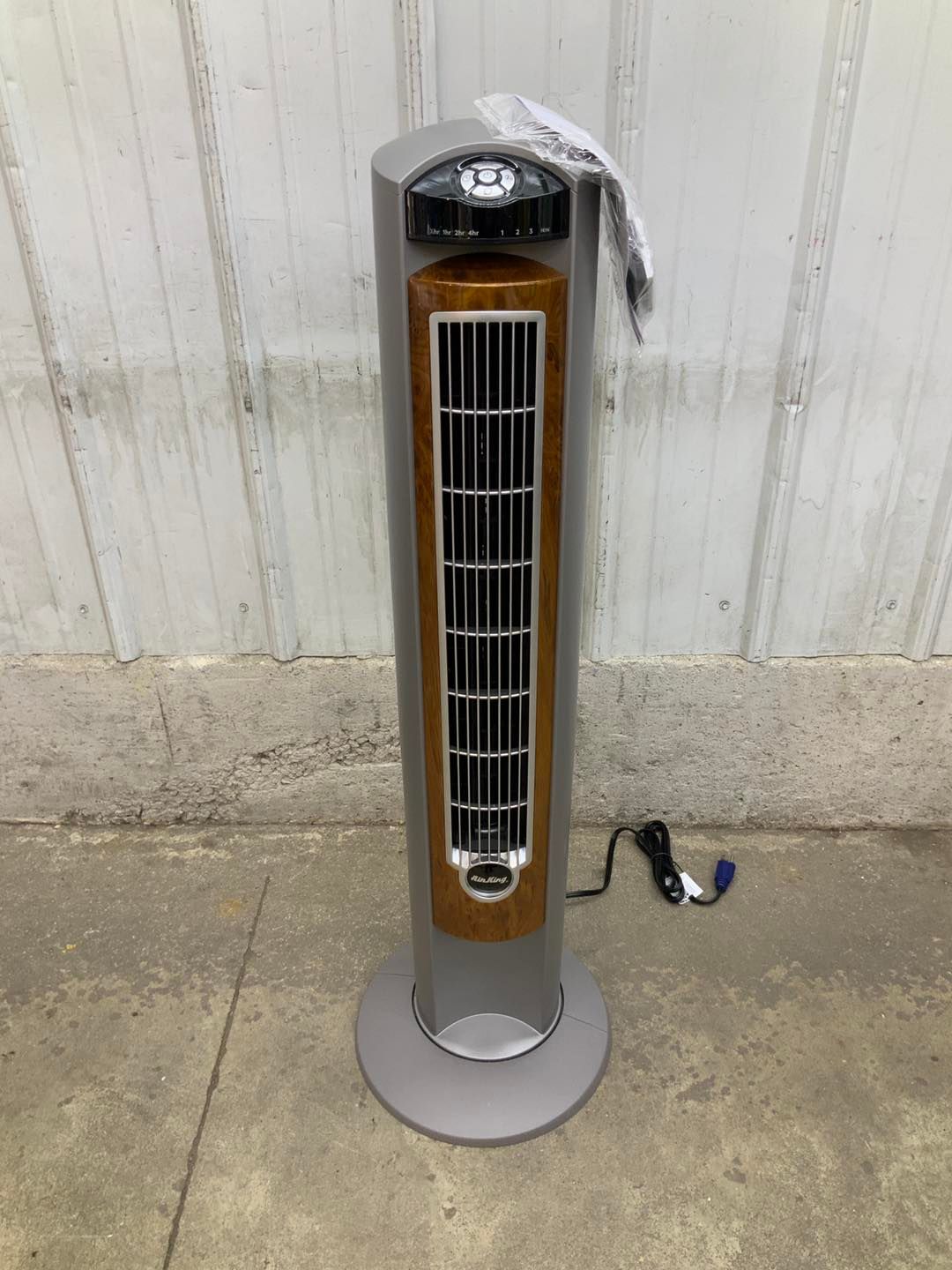 A tower fan is sitting on the ground in front of a white wall.