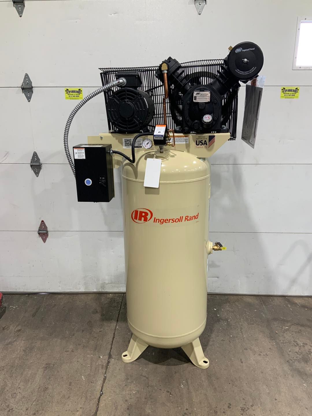 A large air compressor is sitting in front of a garage door.