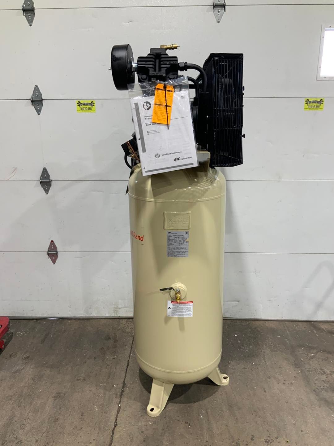 A large air compressor is sitting in front of a garage door.