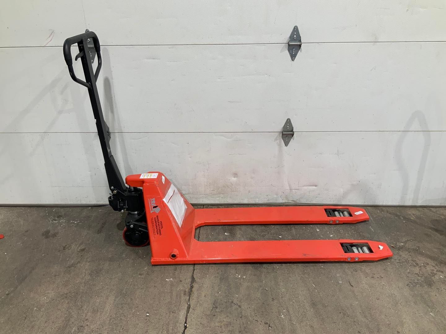 A red pallet truck is sitting in front of a garage door.