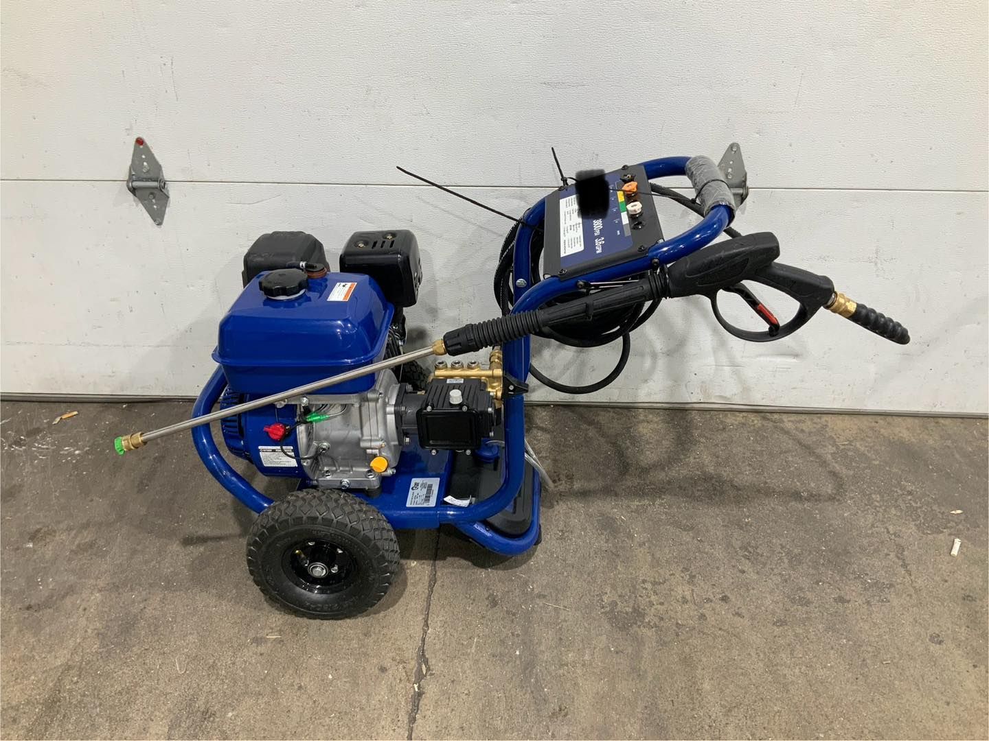 A blue gas powered pressure washer is sitting in front of a garage door.
