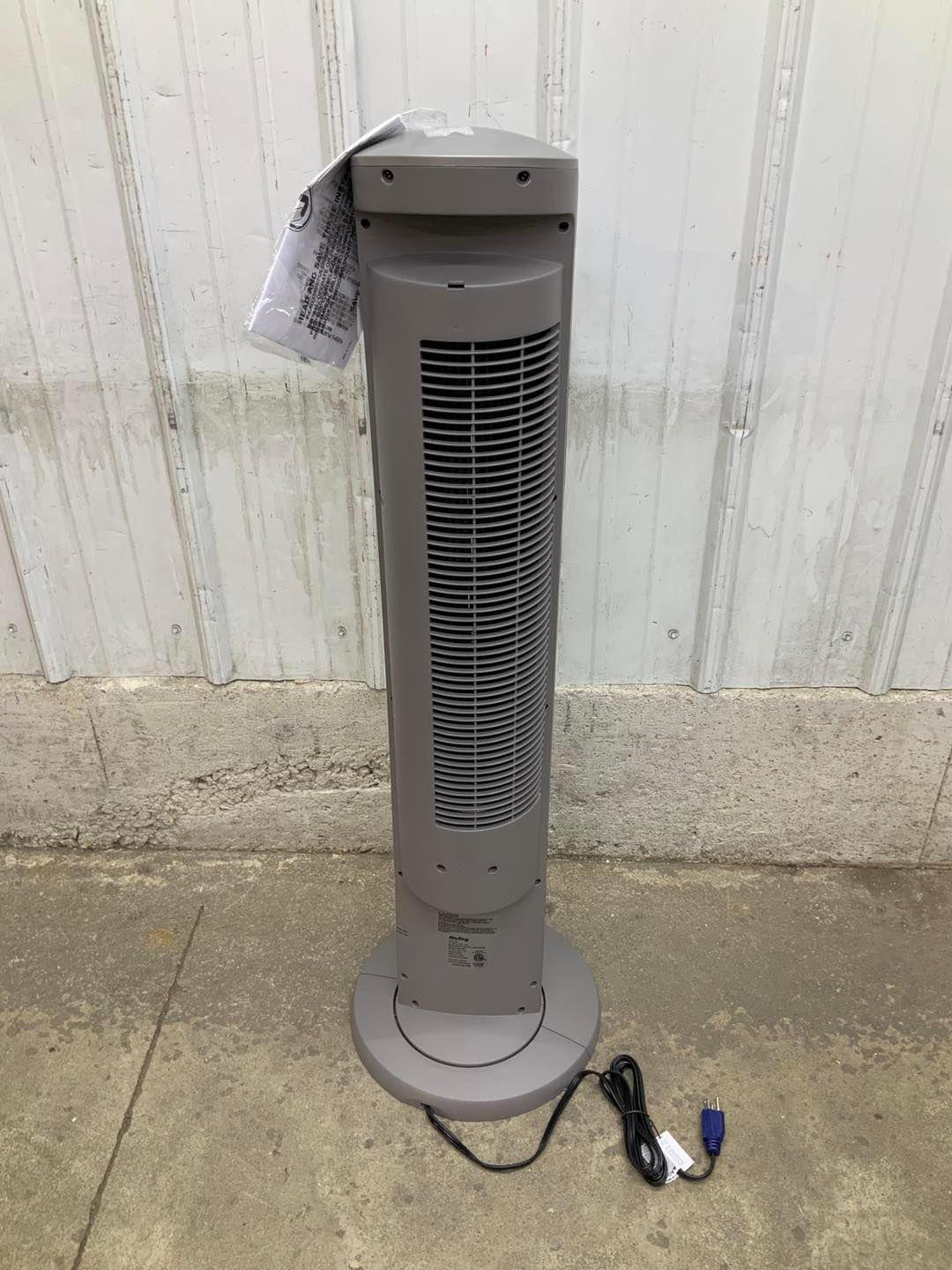 A tower fan is sitting on the ground in front of a white wall.