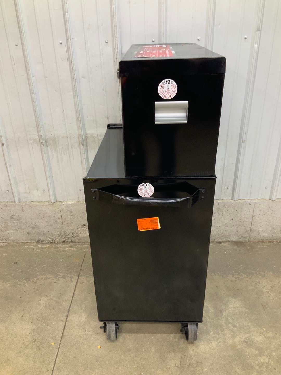 Two black boxes are stacked on top of each other on a concrete floor.
