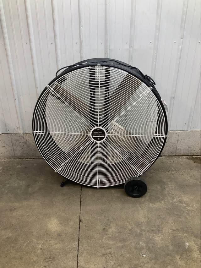 A large fan with wheels is sitting on the ground in front of a building.
