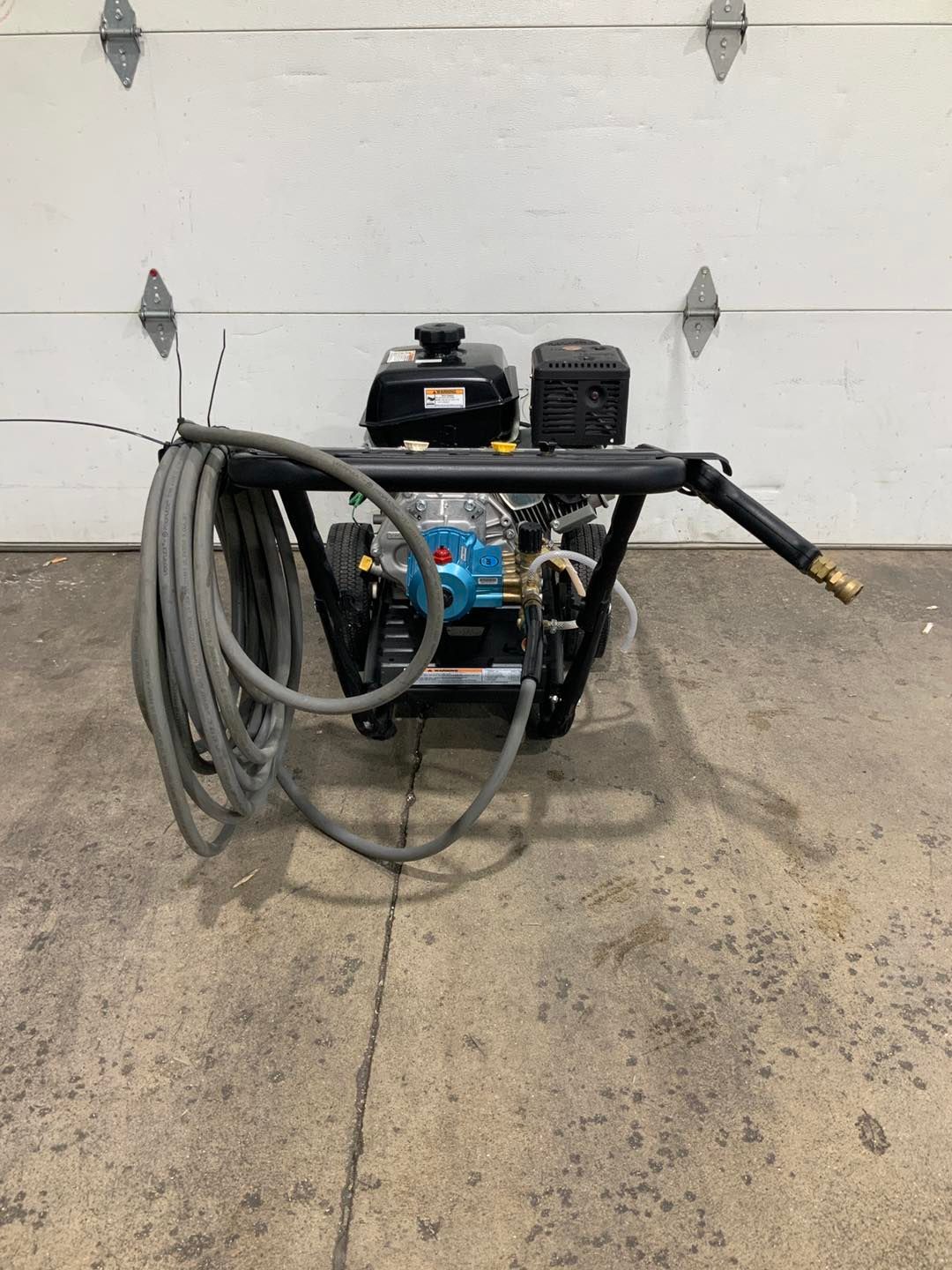A gas powered pressure washer with a hose attached to it is sitting in front of a garage door.