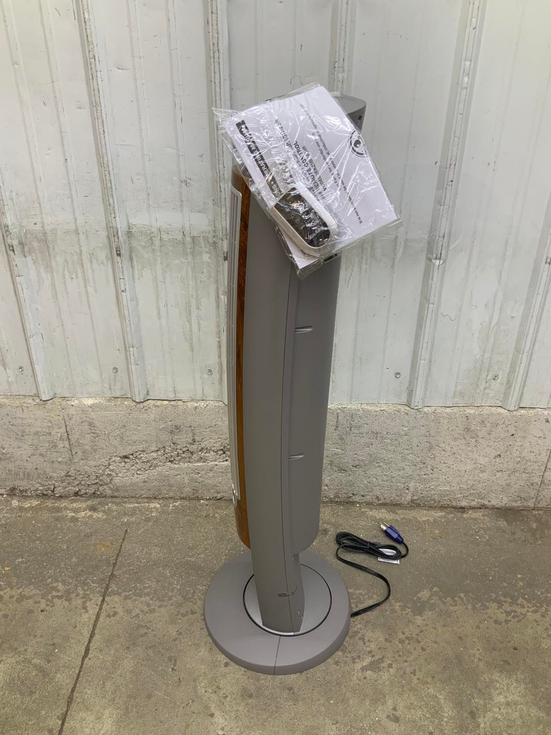 A tower fan is sitting on the ground next to a wall.