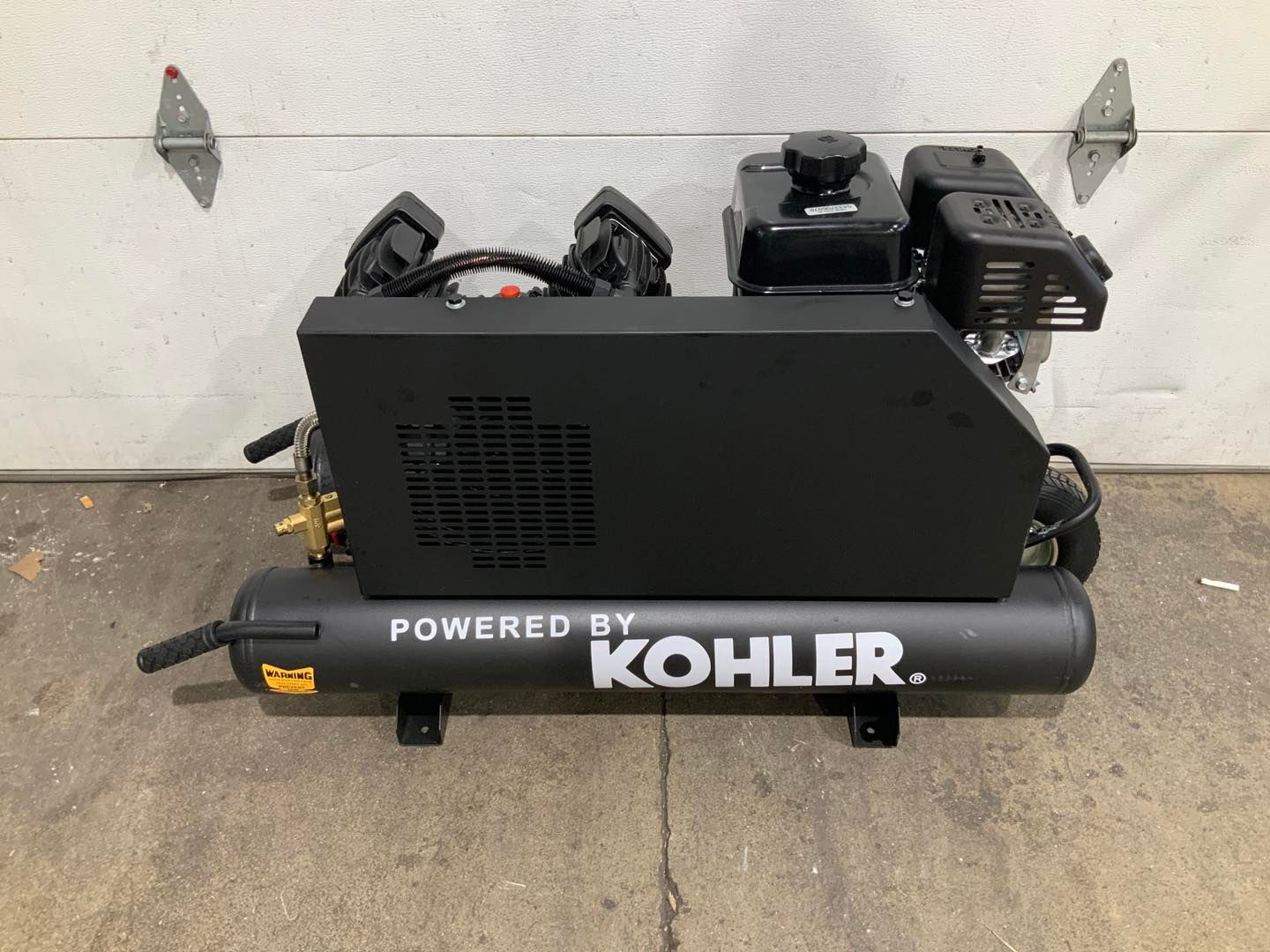 A kohler air compressor is sitting in front of a garage door
