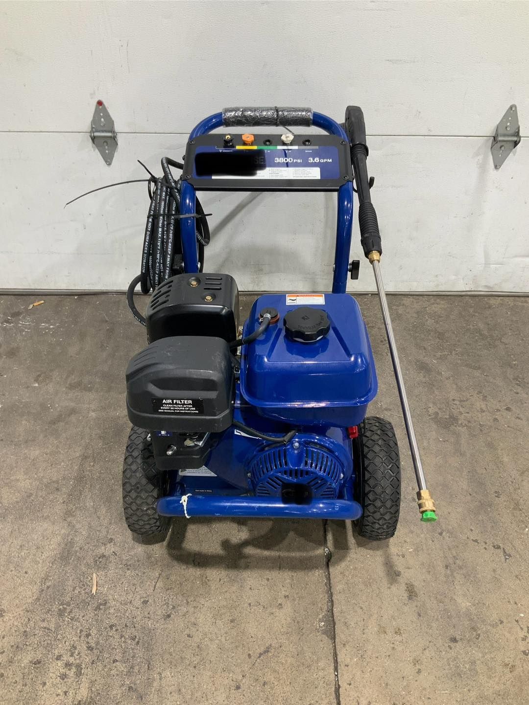 A blue gas powered pressure washer is sitting in front of a garage door.