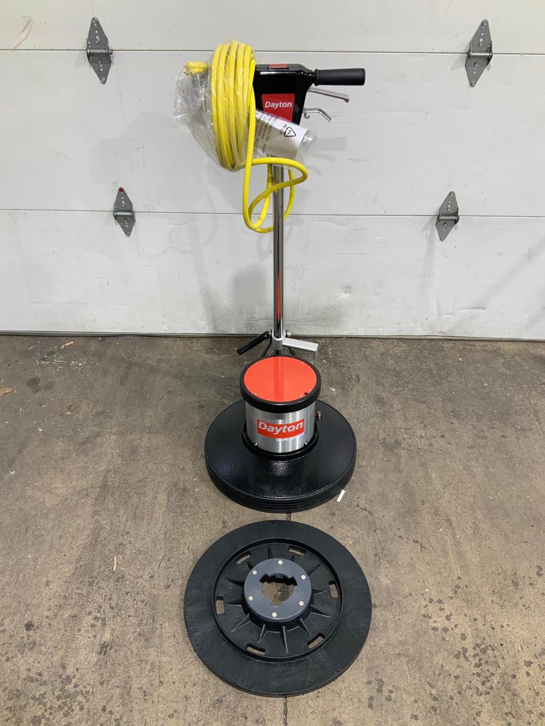 A floor polisher is sitting on the ground next to a garage door.