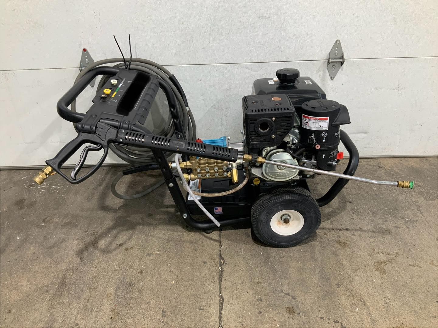 A gas powered pressure washer is sitting on the ground in front of a garage door.