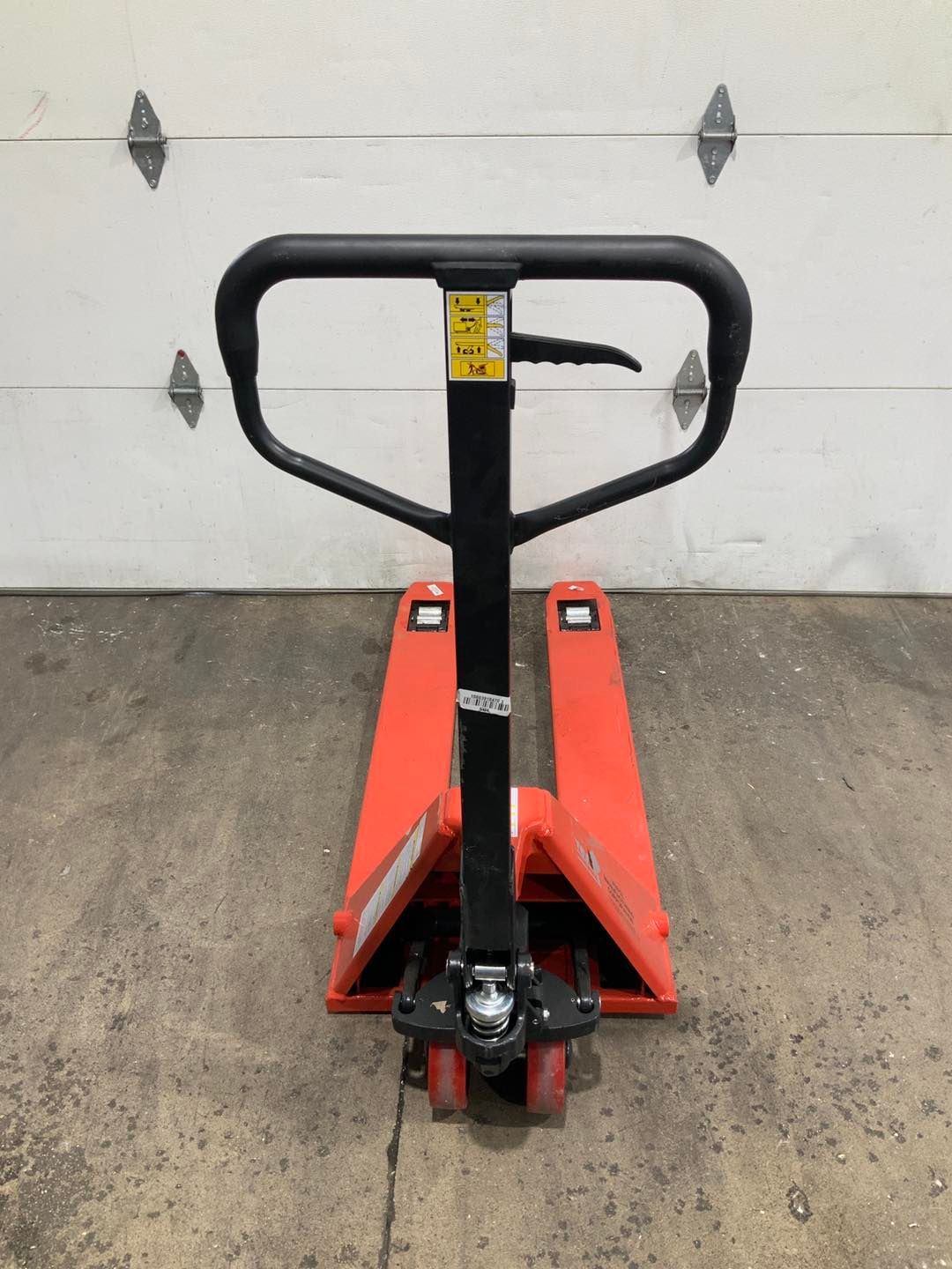A red pallet truck is sitting in front of a garage door