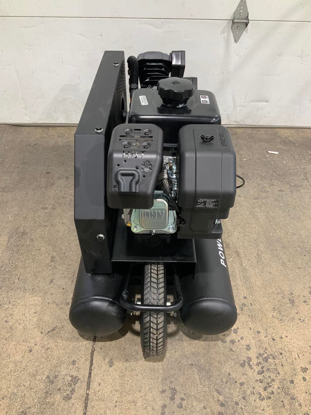 A black air compressor is sitting on a cement floor next to a garage door.