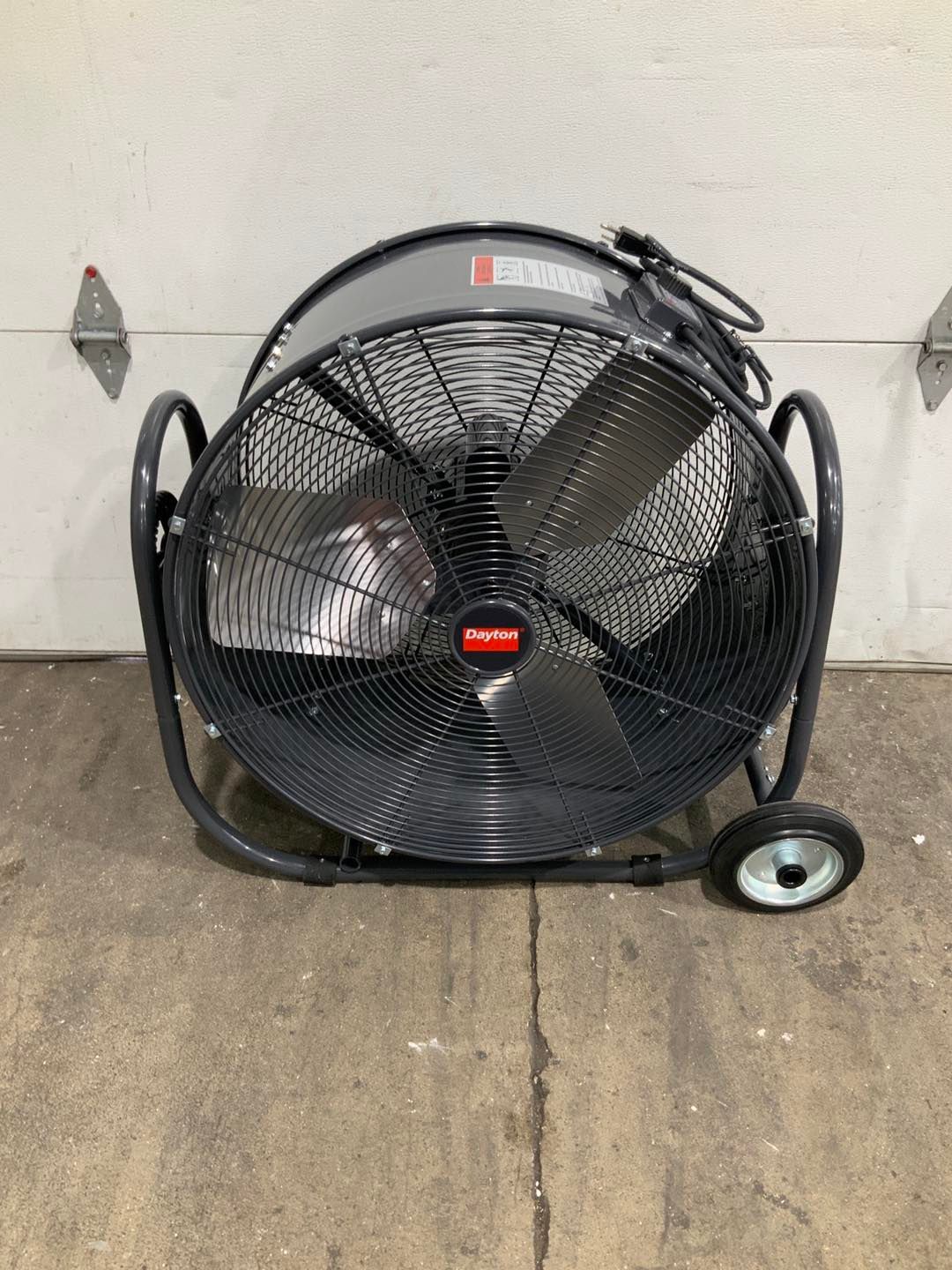 A large fan with wheels is sitting on the ground in front of a garage door.