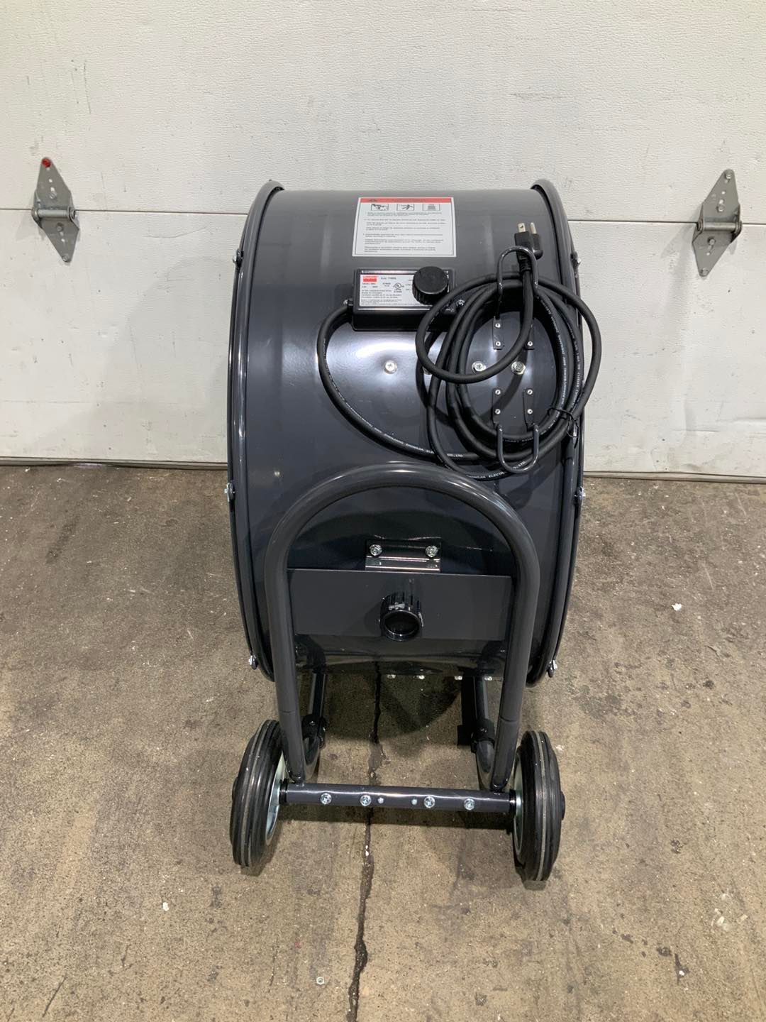 A black blower with wheels is sitting on the ground in front of a garage door.