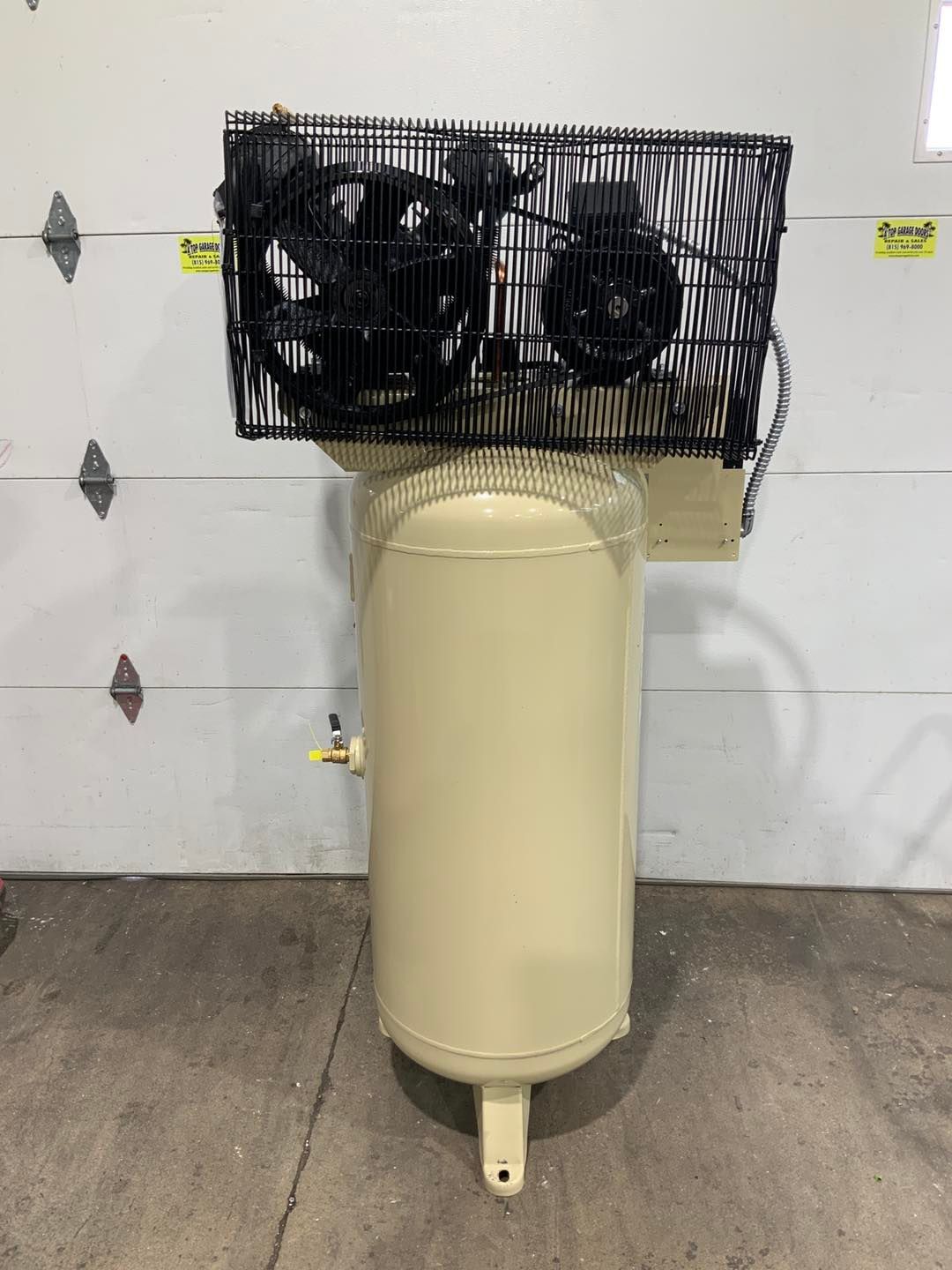 A large air compressor is sitting in front of a garage door.