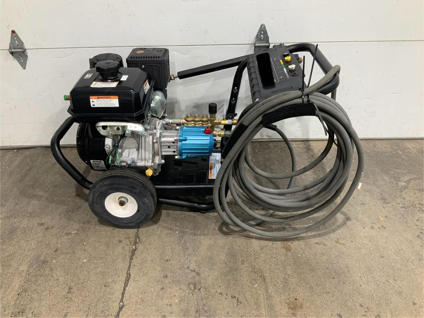 A gas powered pressure washer with a hose attached to it is sitting in front of a garage door.