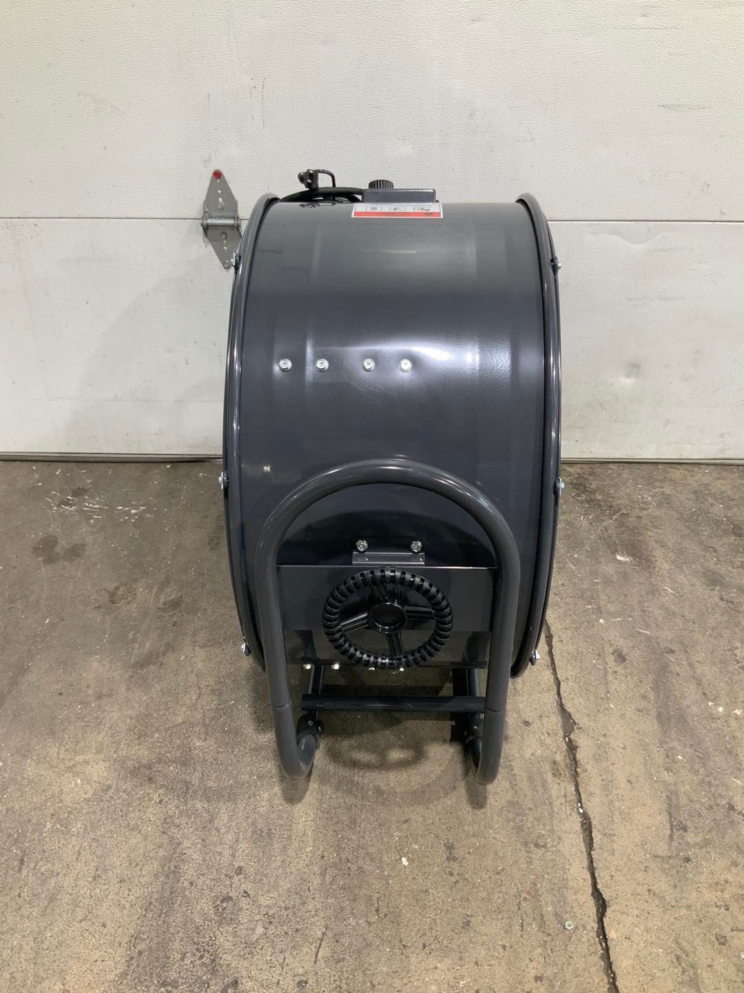 A gray fan is sitting on a concrete floor in front of a garage door.