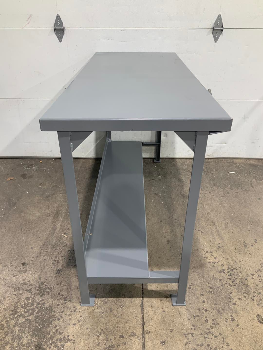A gray table with a shelf underneath it is sitting in front of a garage door.