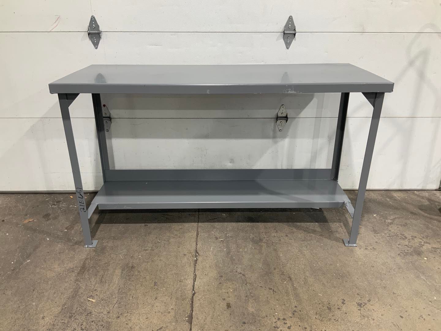 A gray metal table with a shelf underneath it is sitting in front of a garage door.