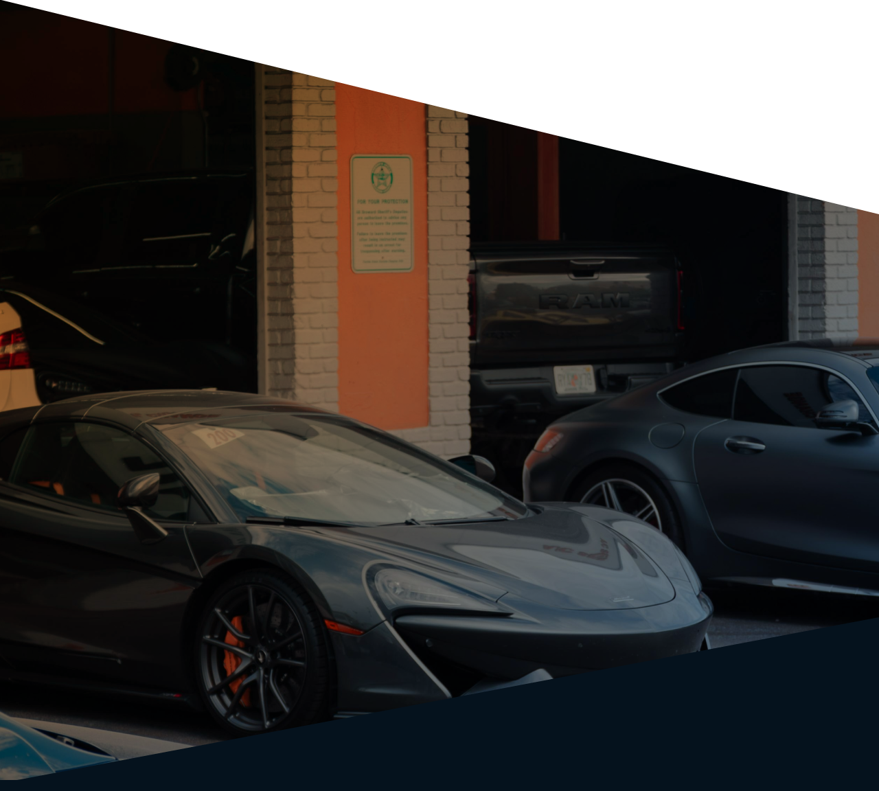 Dark gray sports car parked in a garage with its hood open, beside another gray coupe. | Sam Smith Performance Car Care Center