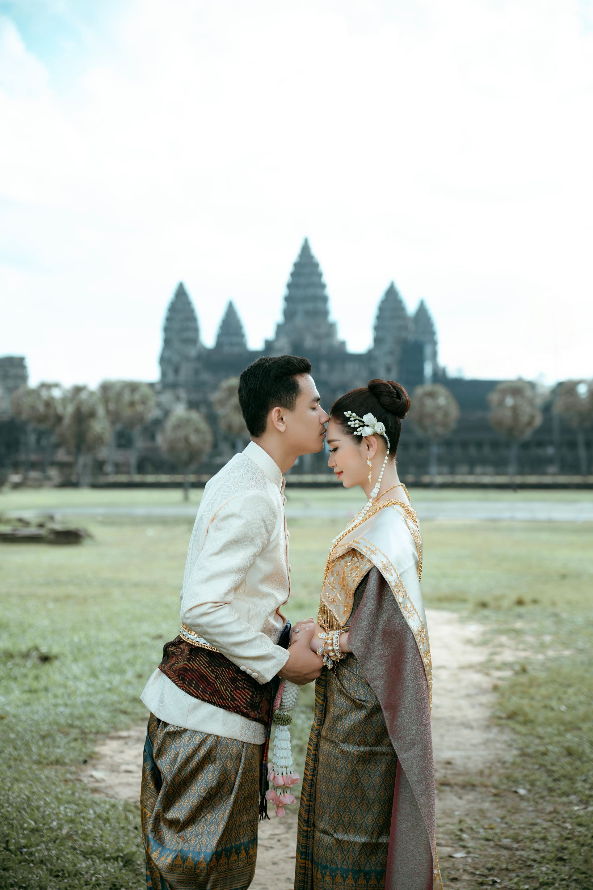 A bride and groom are kissing in front of a temple.