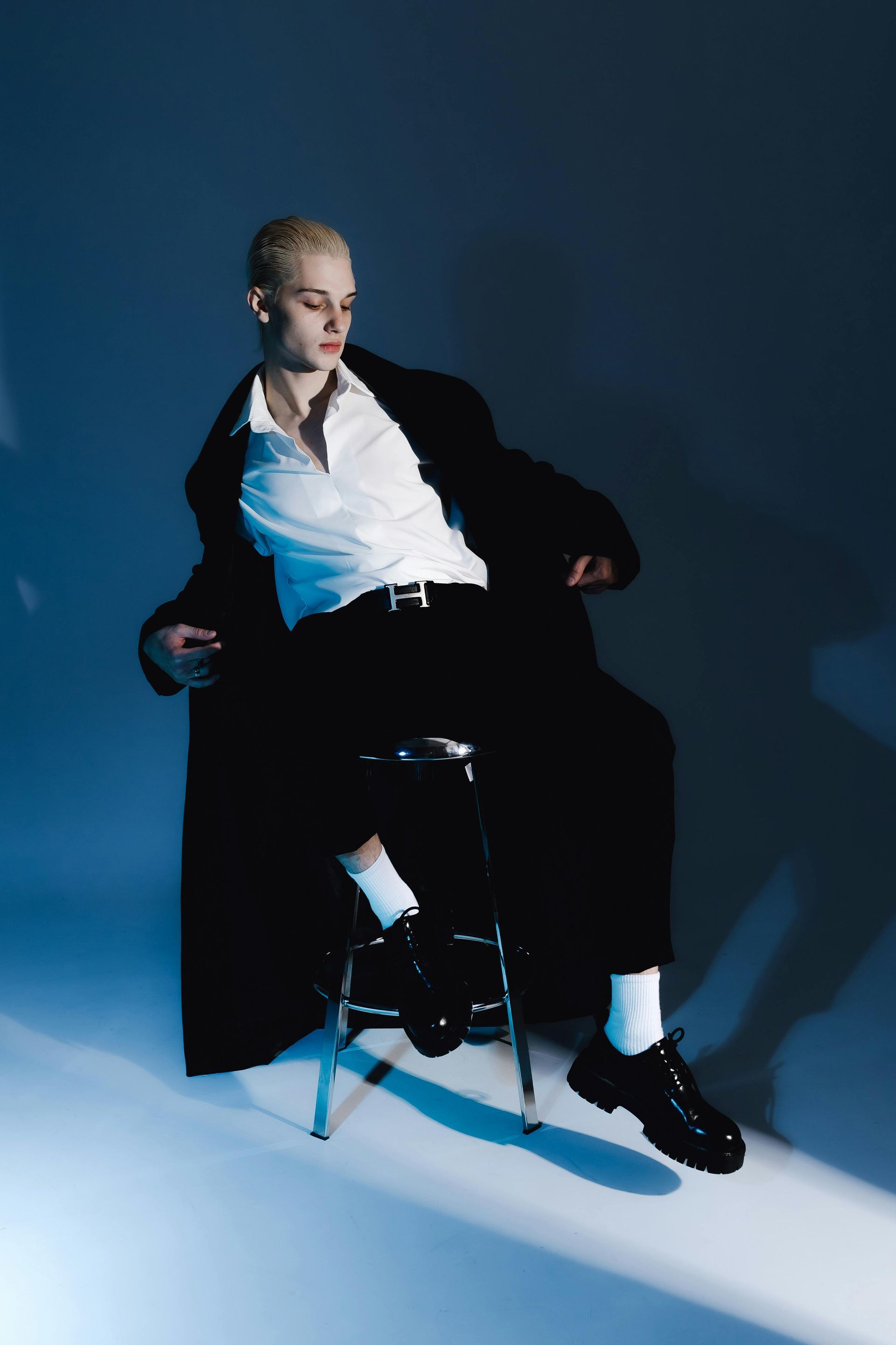 A man in a black coat and white shirt is sitting on a stool.
