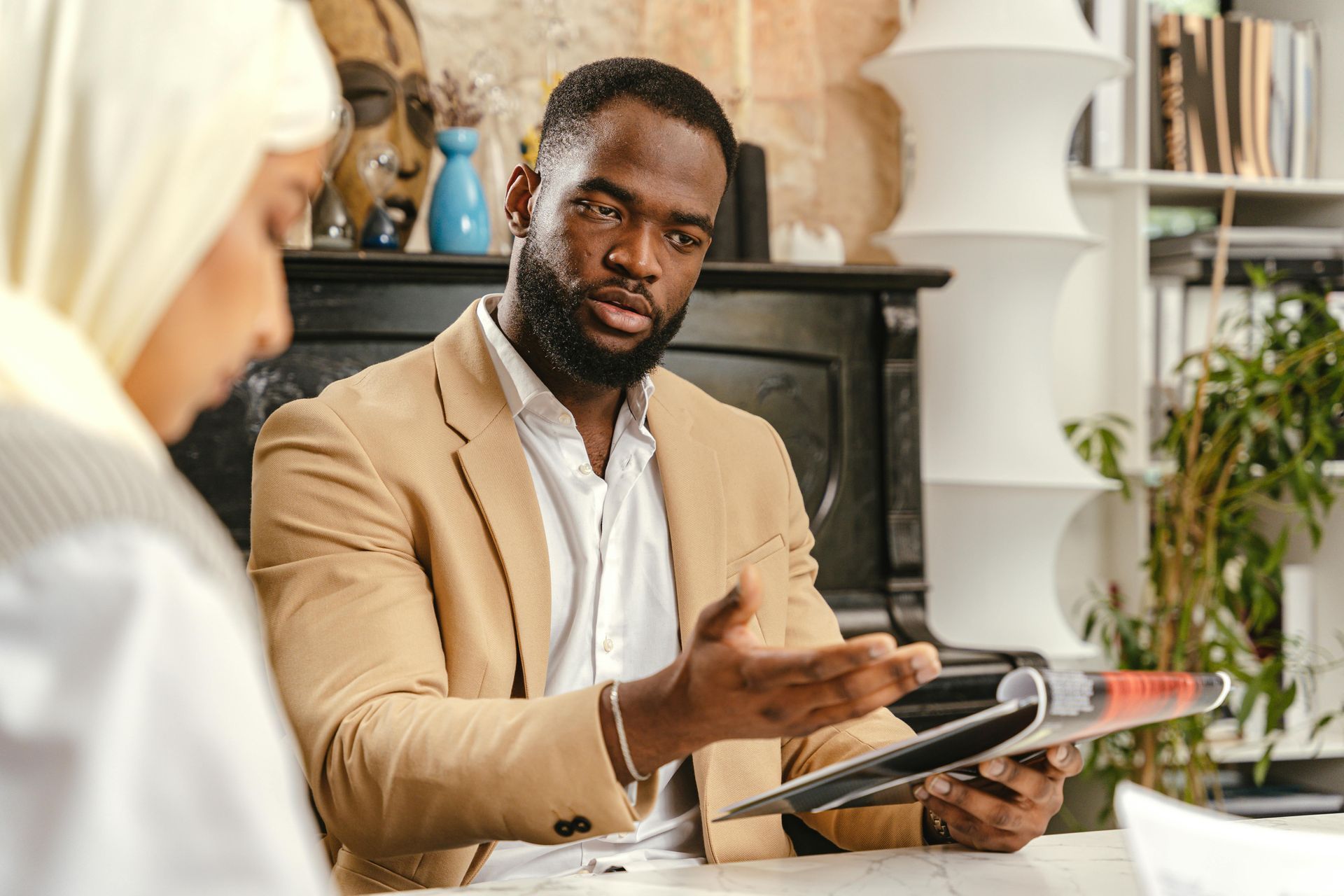 A man is sitting at a table talking to a woman while holding a magazine.