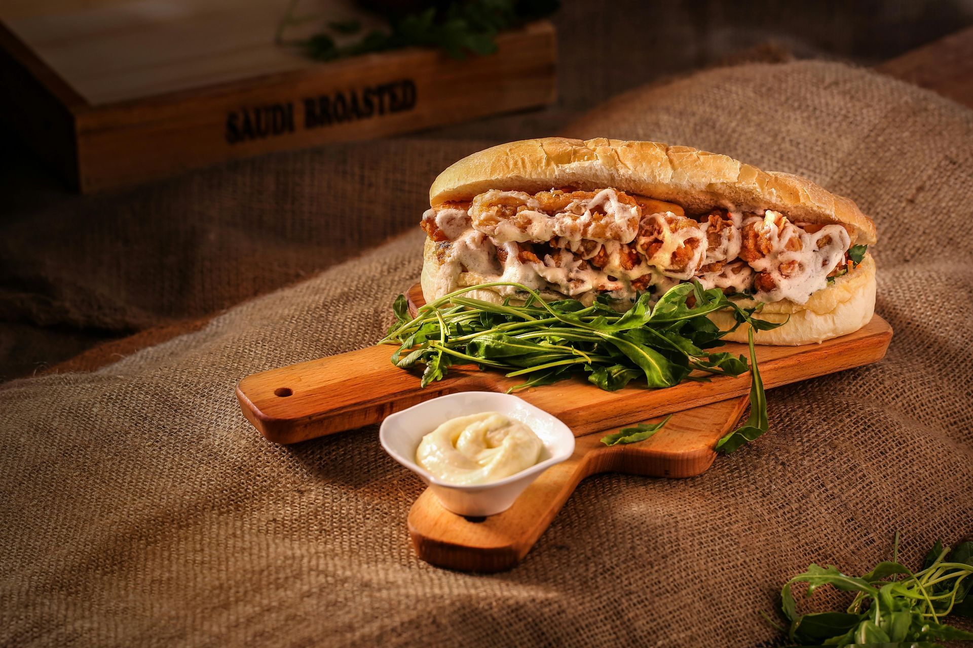 Un sandwich est posé sur une planche à découper en bois à côté d'un bol de mayonnaise.