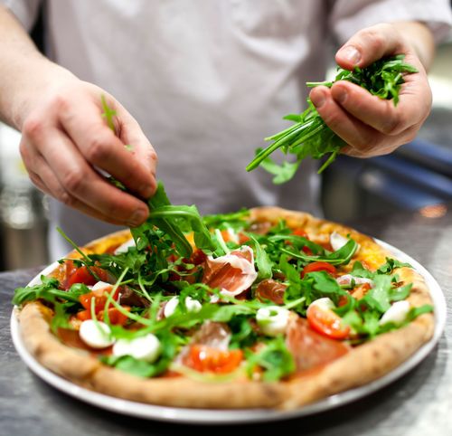 Une personne met des légumes verts sur une pizza dans une assiette