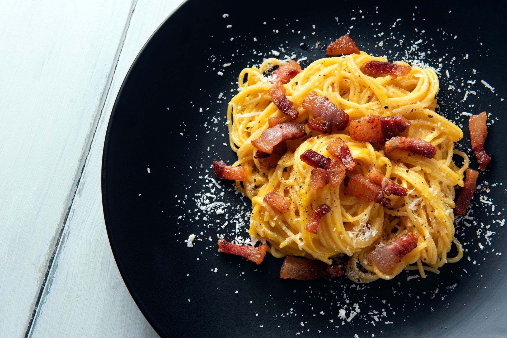 Une assiette noire garnie de spaghetti et de bacon sur une table.
