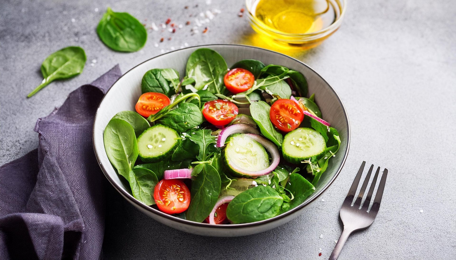 Une salade avec des épinards, des tomates, des concombres, des oignons et de l'huile d'olive dans un bol avec une fourchette.