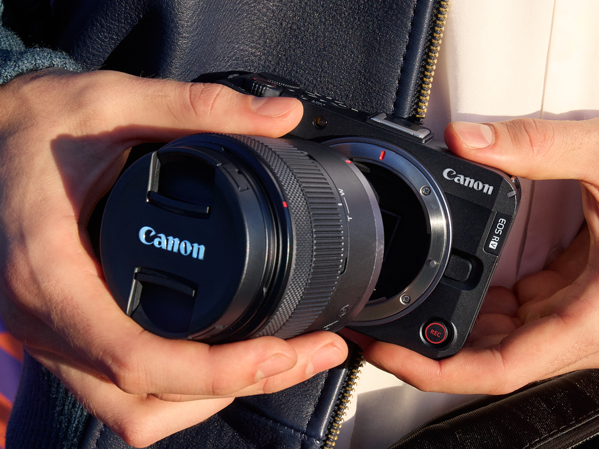 person mounting lens on Canon EOS R50 V mirrorless camera