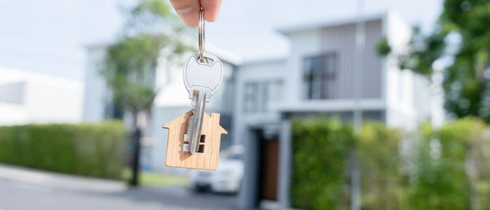 A person is holding a house key in front of a house.