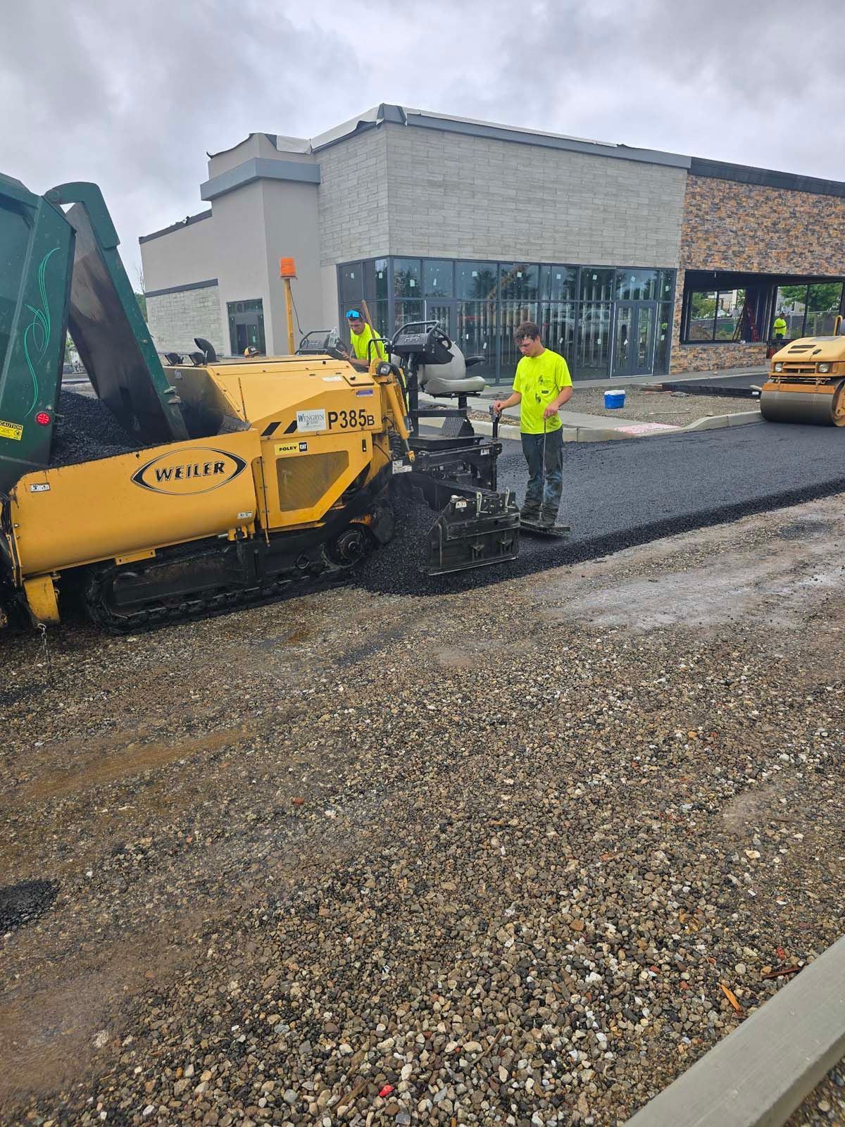 A man is standing next to a machine that is paving a road.