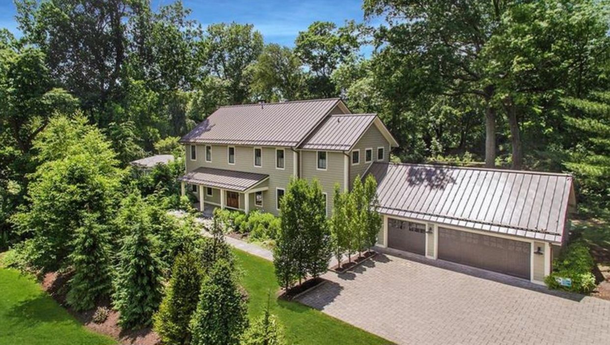 An aerial view of a large house with a metal roof surrounded by trees.