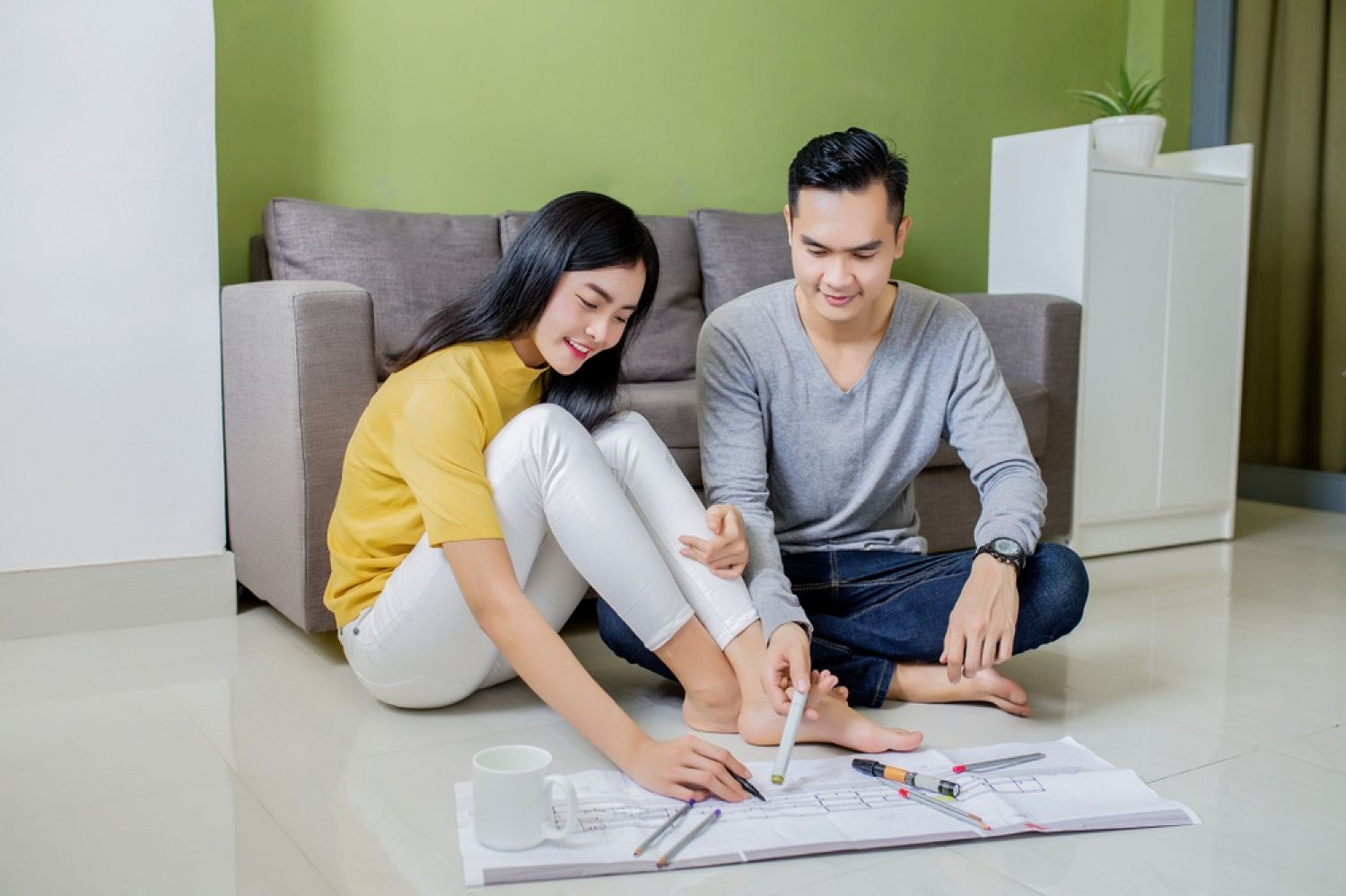 A man and a woman are sitting on the floor looking at a blueprint.