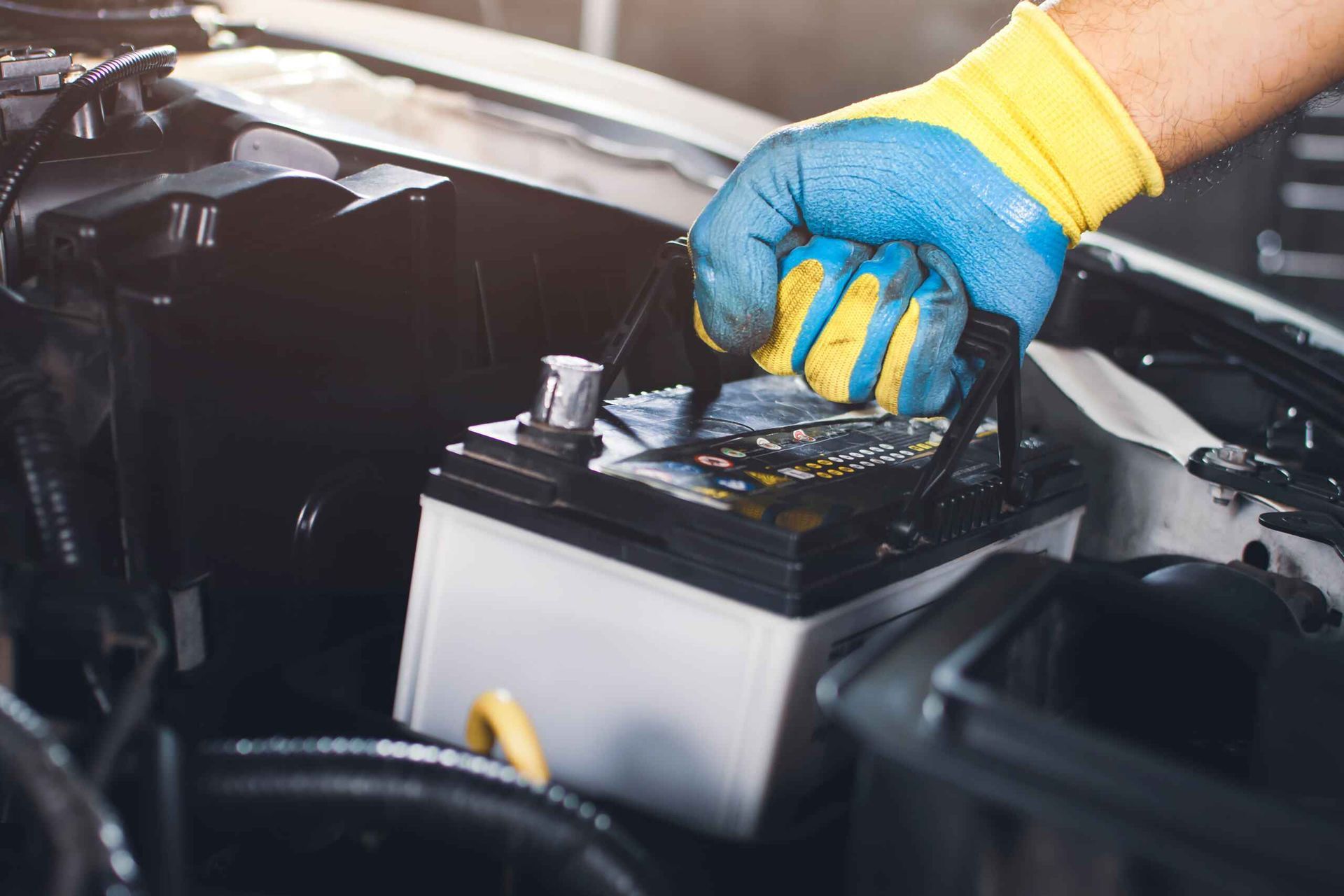 A Person is Holding a Battery in Their Hand While Working on a Car — Central Coast Batteries In Long Jetty, NSW