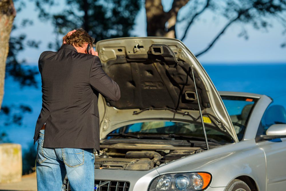 A Man is Looking Under the Hood of a Broken Down Car — Central Coast Batteries In Tuggerah Lake, NSW
