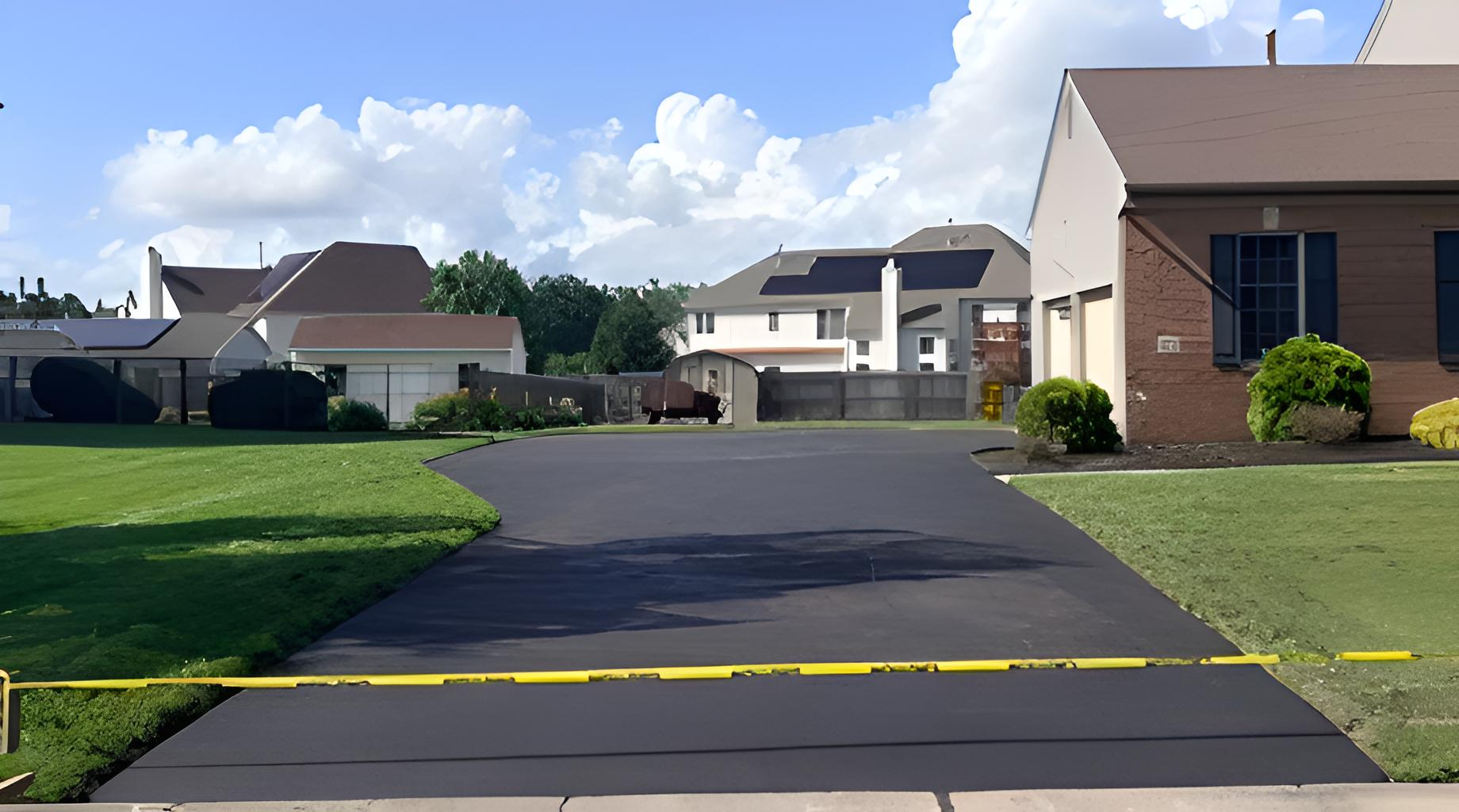 Suburban street with houses, green lawns, and a yellow caution tape blocking newly paved asphalt driveway