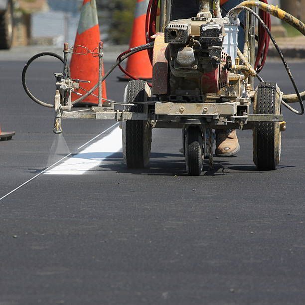 Road-marking machine painting a white line on asphalt beside orange traffic cones