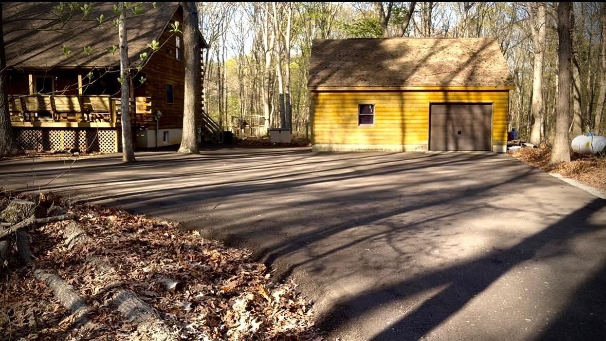 Brown garage in a wooded driveway with long tree shadows across the driveway