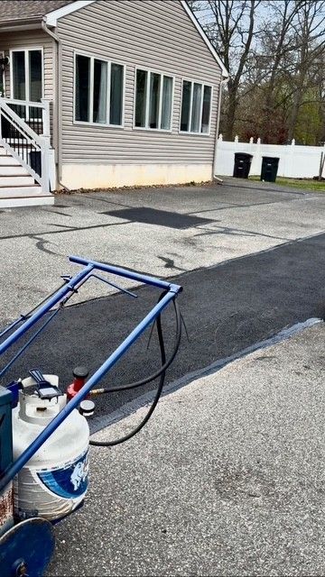 Driveway beside a house with a propane crack filling machine setup and black asphalt patching in progress