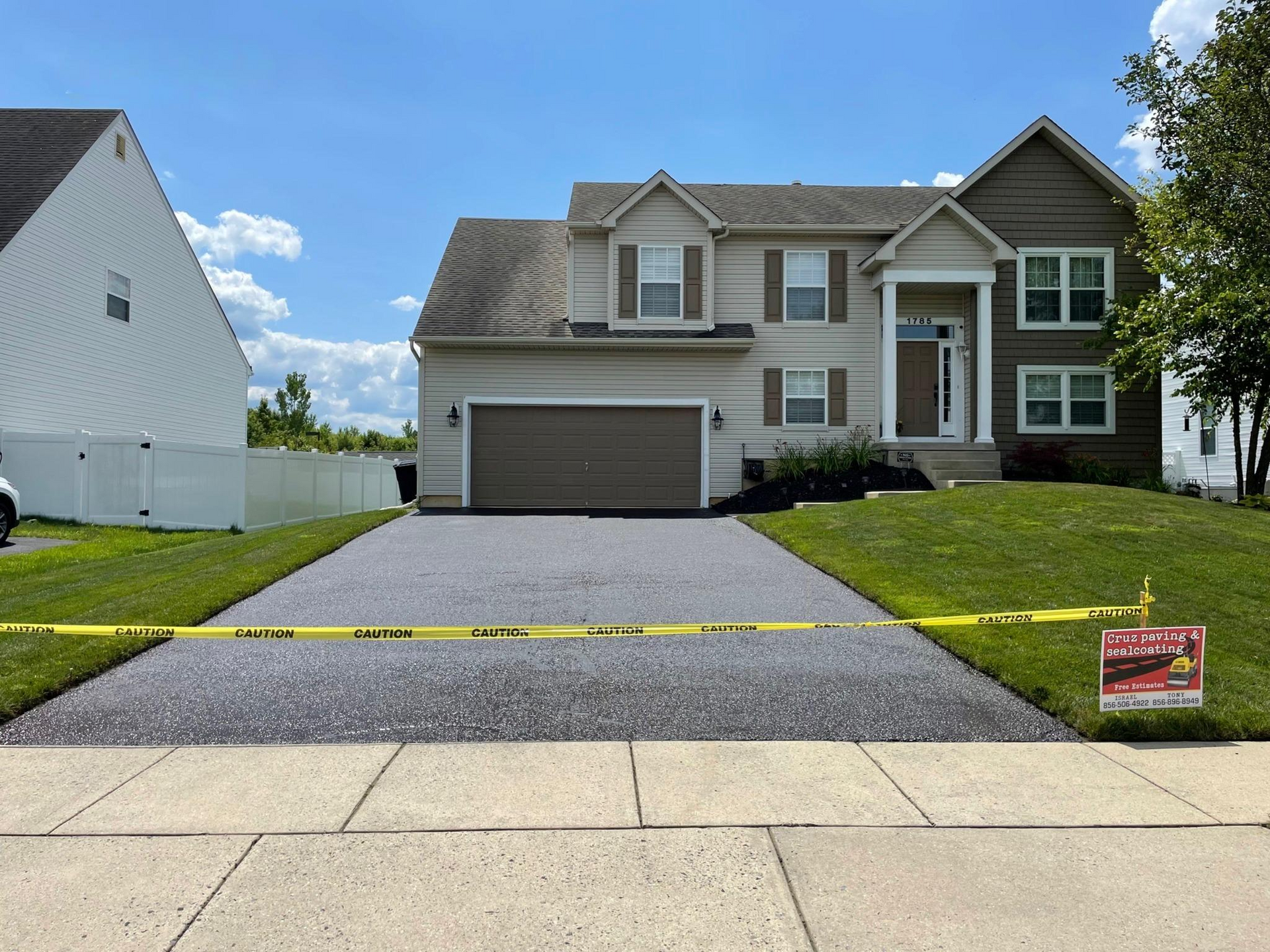 Suburban house with attached garage, gray siding, and a Cruz Paving & Sealcoating sign in the front yard