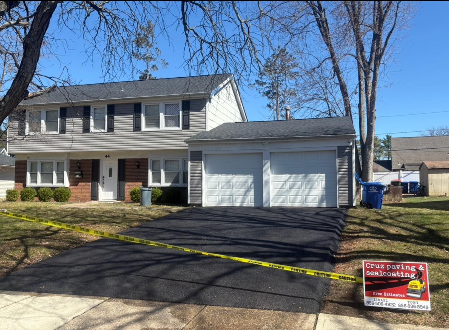 Two-story suburban house with white garage, black driveway, and yellow caution tape across the front yard