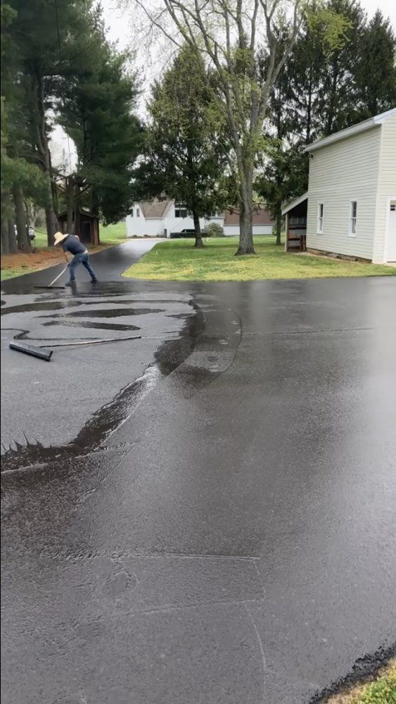 Cruz Paving & Sealcoating employee spreading sealcoating application across asphalt driveway