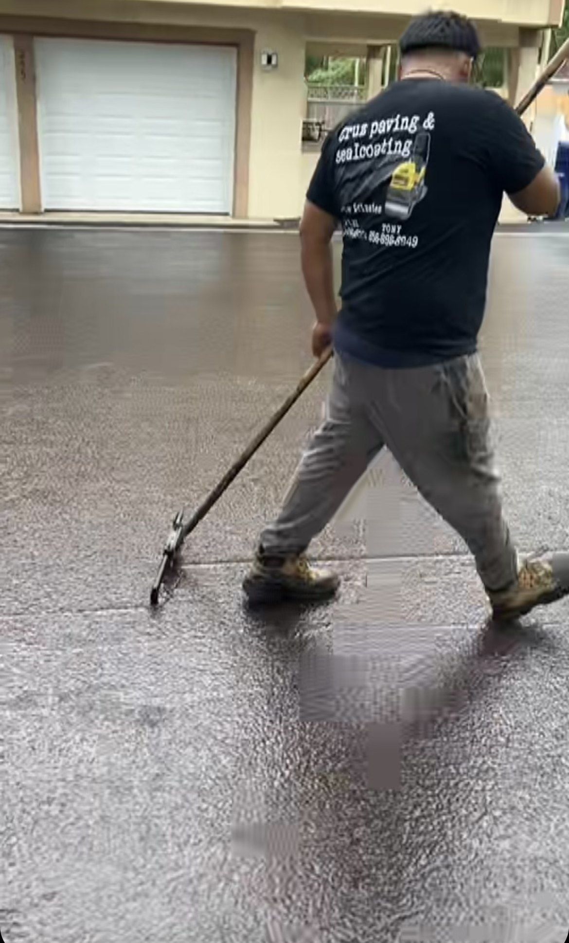 Cruz Paving & Sealcoating employee using a long-handled squeegee to spread a sealcoating application across an asphalt driveway