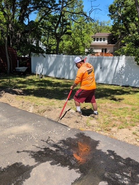 Cruz Paving & Sealcoating employee in orange safety vest using a shaping rake to remove dirt from next to asphalt driveway