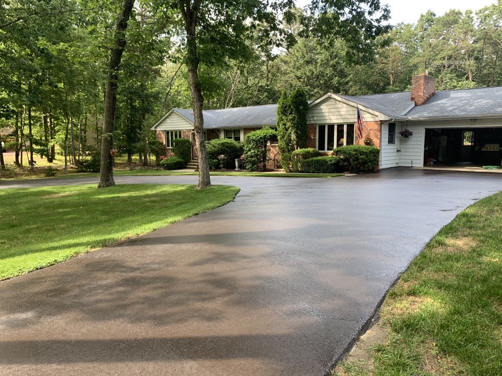 Curved, sealcoated driveway leading to a house with trees and a well-kept lawn in front
